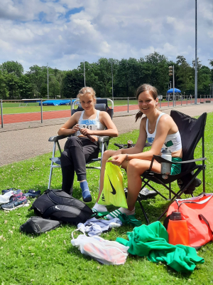 Malou en Anouk zitten op twee stoelen naast de baan en lachen in camera